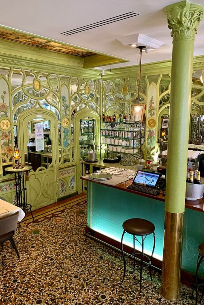 Art Nouveau interior of a café with intricate designs and a mosaic floor.
