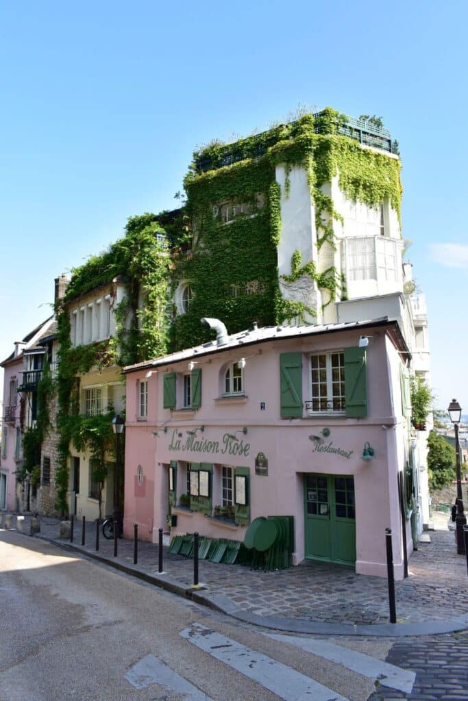 Quaint corner building covered in greenery with the sign "La Maison Rose" in Montmartre.