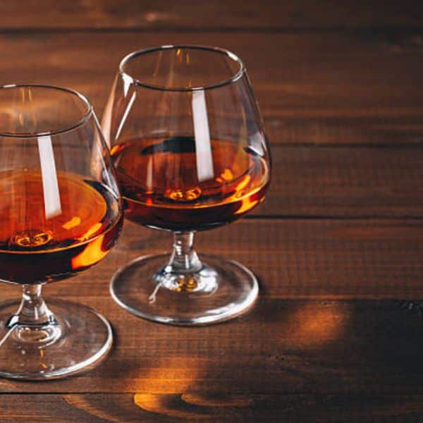 Two snifter glasses filled with amber-colored Armagnac brandy, set on a wooden table reflecting warm light.