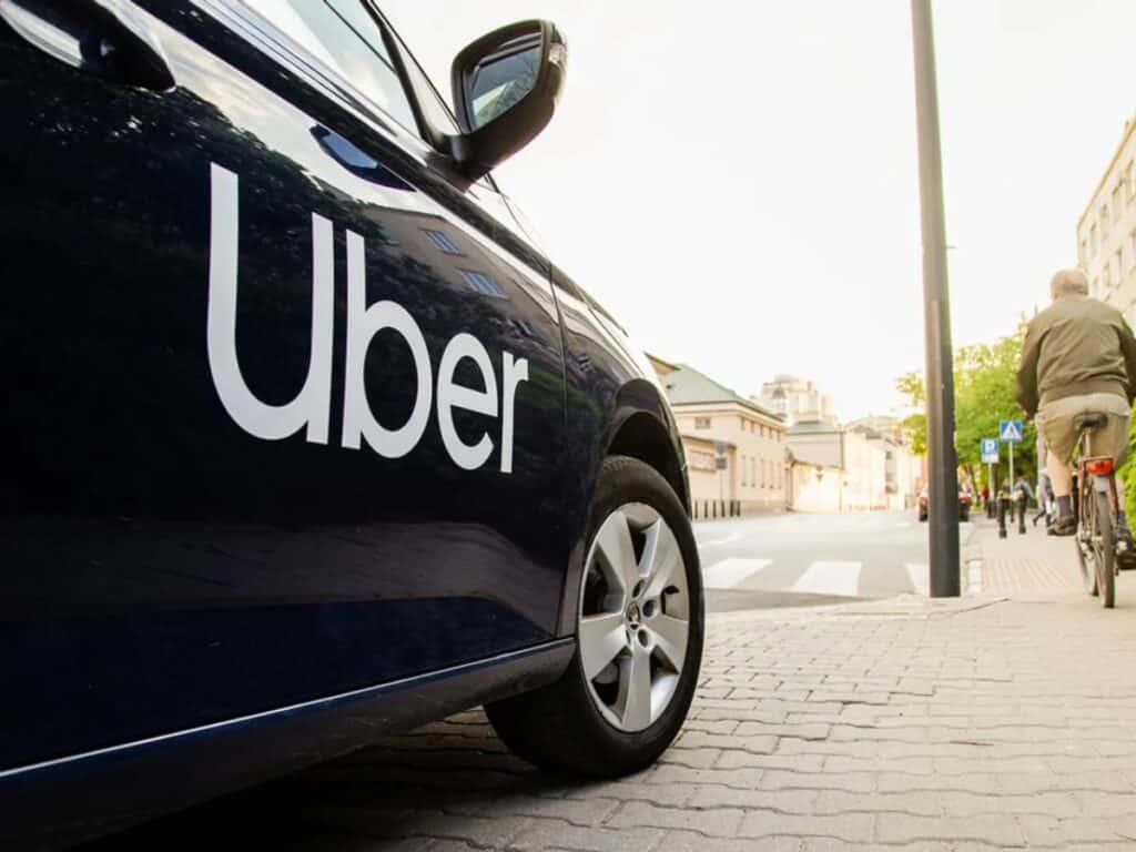 A black taxi with the word UBER on the side driving on a street in Paris.