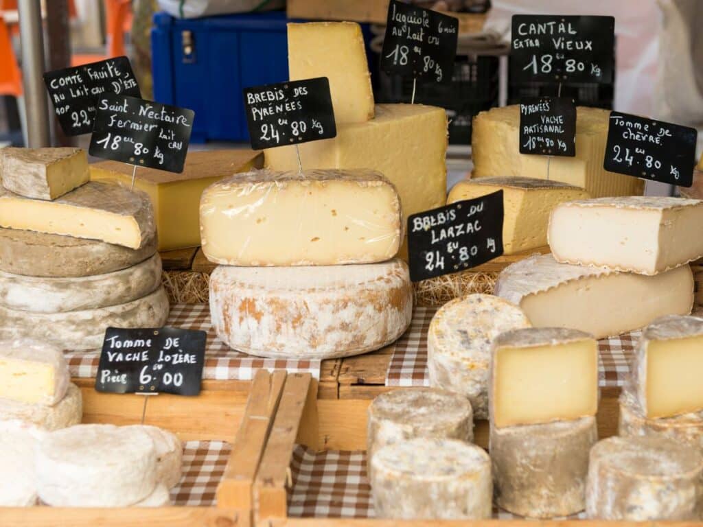 Various types of cheese displayed at a market, with handwritten labels showing prices per kilogram in euros.