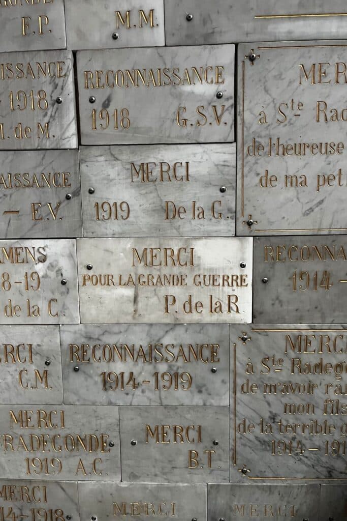 Close-up of ex-voto plaques on the wall, including a plaque thanking Sainte Radegonde for protection during the Great War (Merci Pour La Grande Guerre).