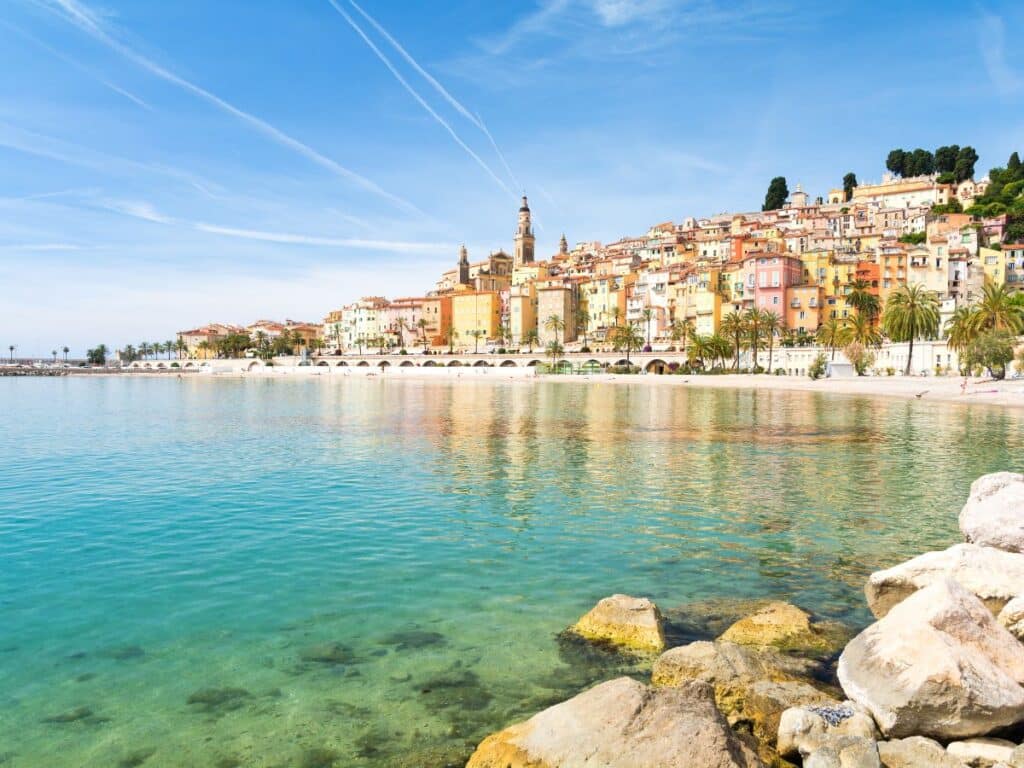 A picturesque coastal town with colorful buildings and a calm, clear sea under a bright blue sky.