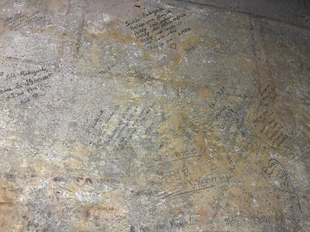 Graffiti messages written on a stone wall, expressing devotion and prayers to Sainte Radegonde, some in the shape of hearts.