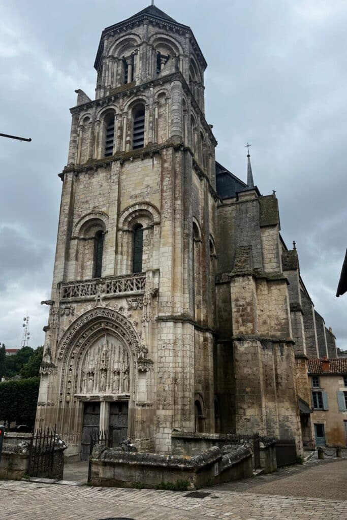 Exterior view of the Church of Sainte Radegonde in Poitiers, showcasing its Romanesque architecture with tall, narrow windows, and ornate carvings above the main entrance.