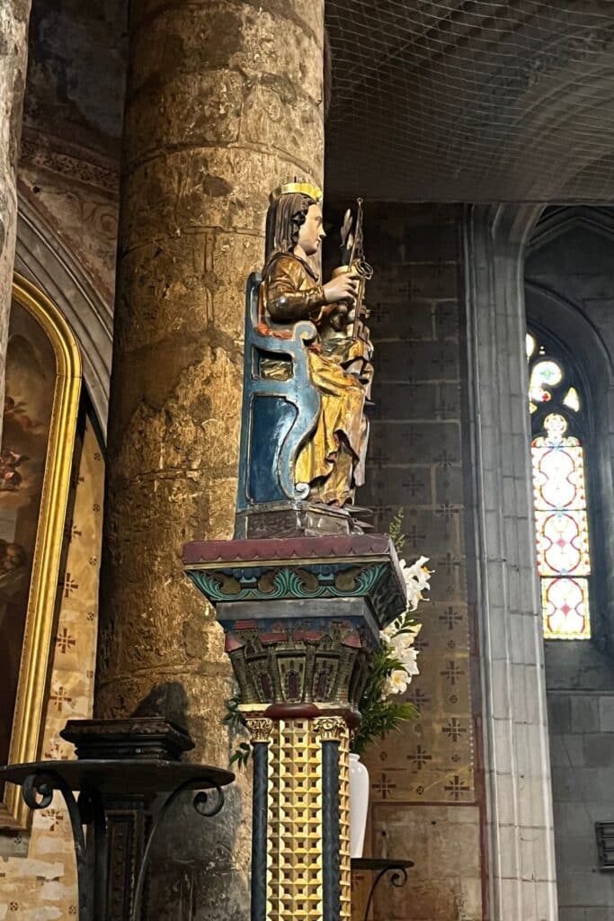 Side view of a statue representing 'The Miracle of the Keys,' featuring a crowned figure seated on an ornate pedestal, holding keys, within a stone church interior.