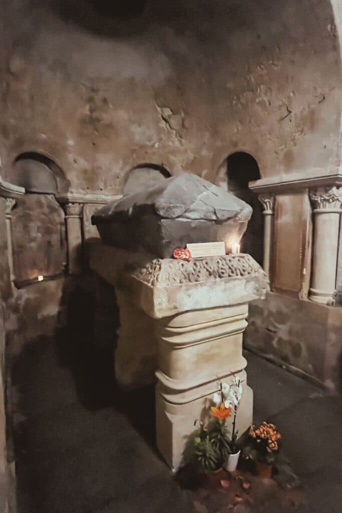 Close-up of the sarcophagus of Sainte Radegonde, located in a dimly lit stone crypt, with flowers and candles placed around the base.