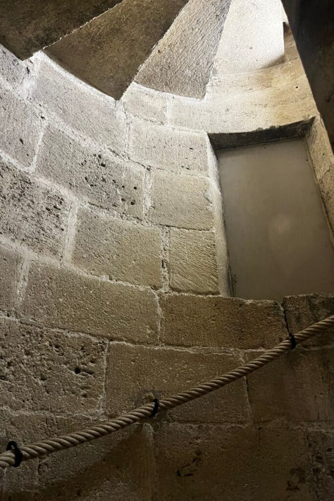 Stone spiral staircase inside the Donjon Gilles Aycelin, showing the textured brick walls and a rope handrail for support.