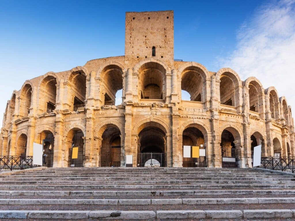 The Arles Amphitheatre, an ancient Roman arena with multiple archways, set against a clear blue sky.