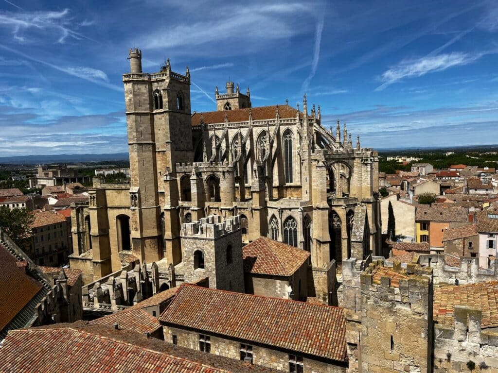 The Donjon Gilles Aycelin in Narbonne, featuring its historic Gothic architecture with intricate stonework, spires, and towers under a clear blue sky.