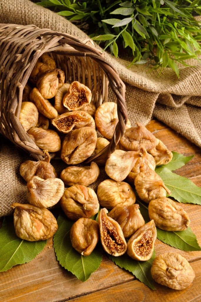 A close-up of dried figs on a wooden platter, with one fig split open to reveal its dense, seedy interior.