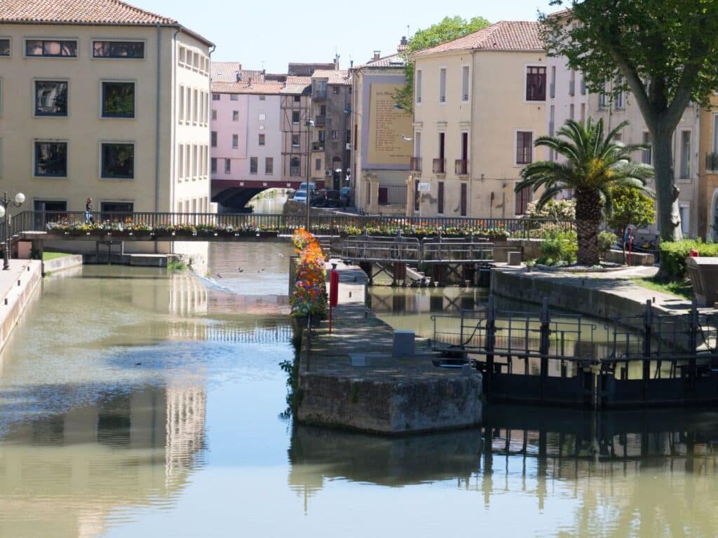 A picturesque canal in Narbonne, France, lined with historic buildings and adorned with vibrant flowers, capturing the charm of the city's waterways and architectural heritage.