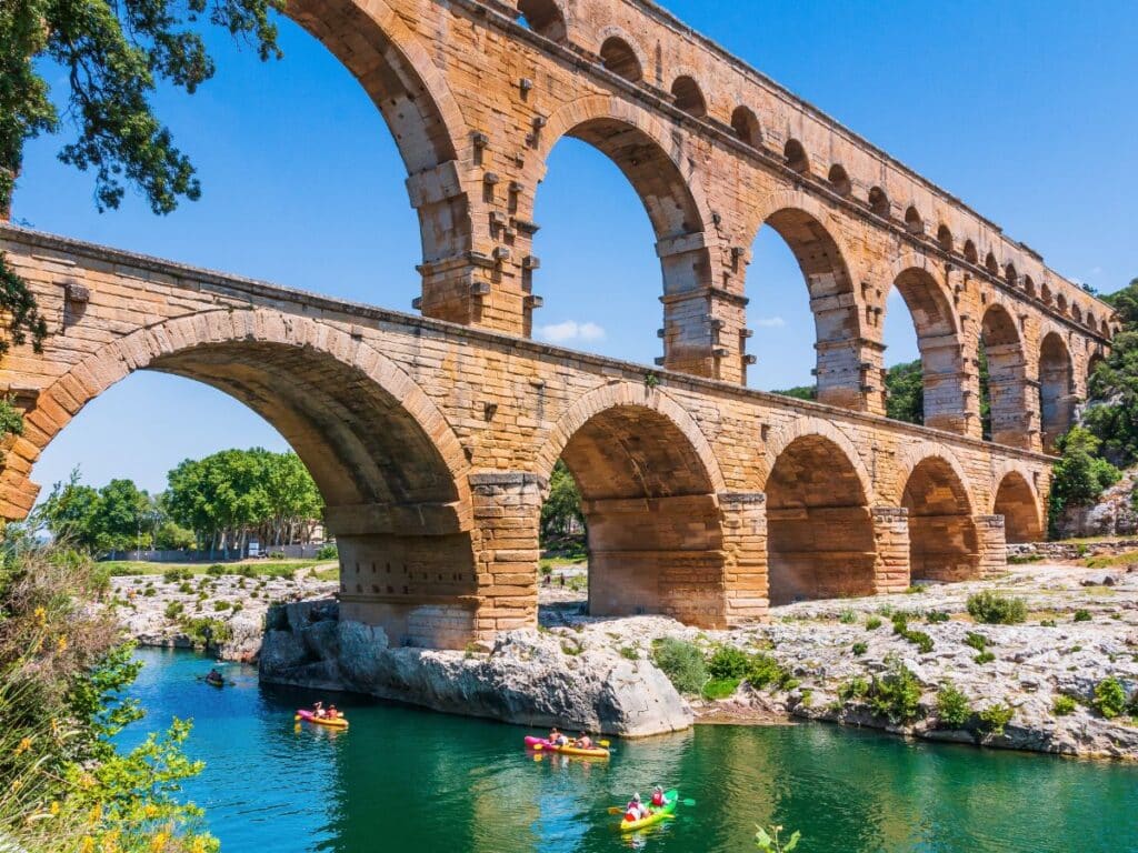 The ancient Roman aqueduct, Pont du Gard, with its multiple arches spanning a river where people kayak below.