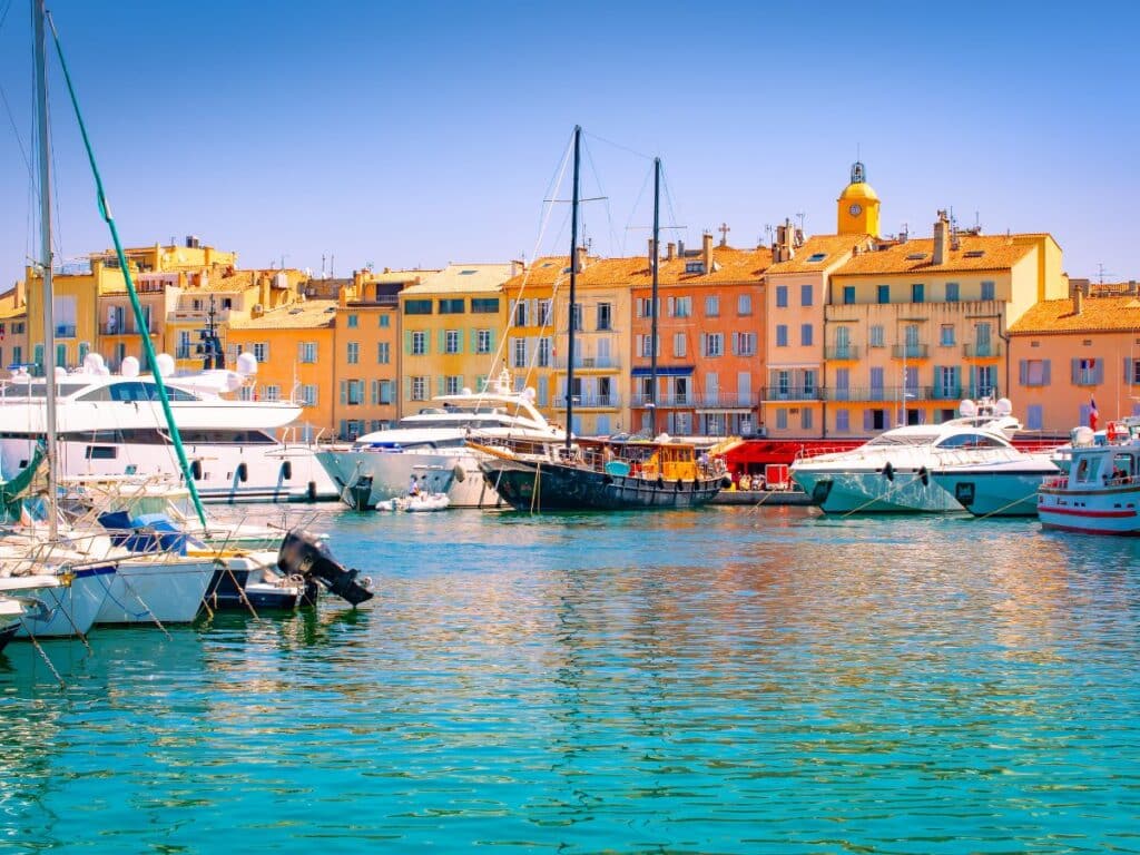 The vibrant port of Saint-Tropez, lined with colorful buildings and filled with yachts and boats under a sunny sky.