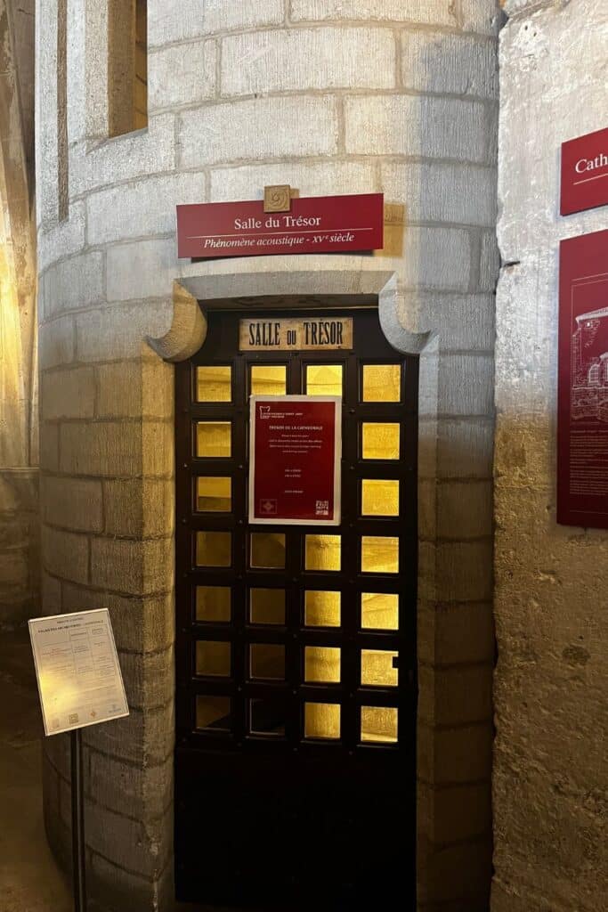 Entrance to the Salle du Trésor at Narbonne Cathedral, marked by a red sign with the room's name and description of its 15th-century acoustic phenomenon.