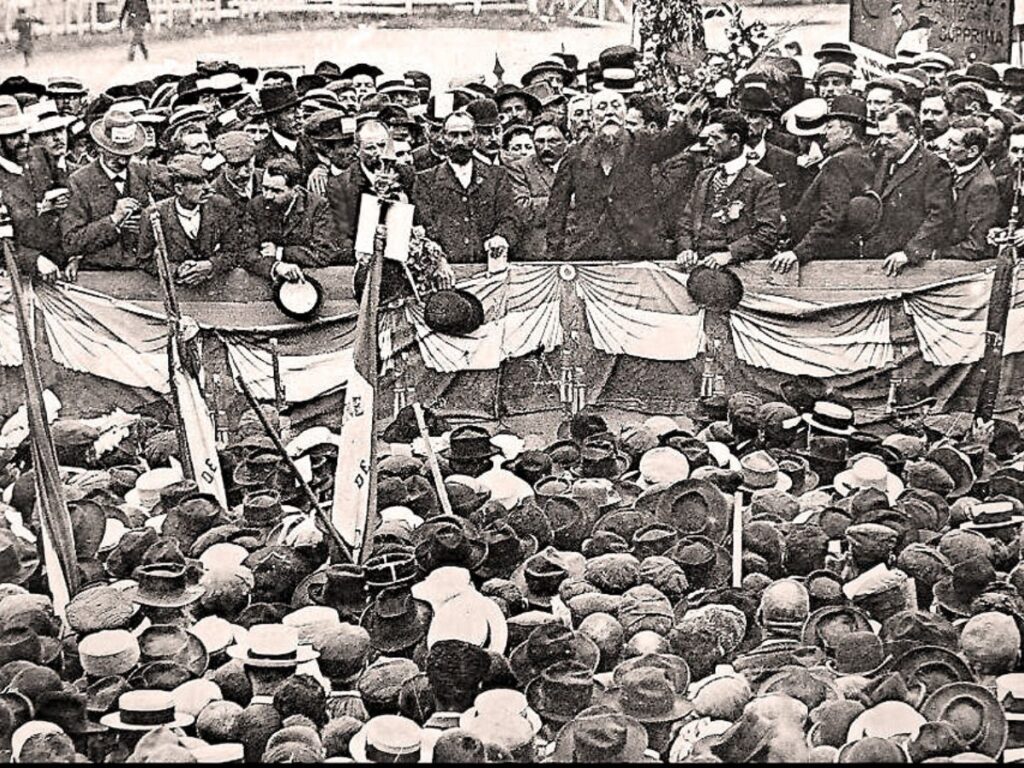 A historical black-and-white photo of a large crowd gathered during a protest in Narbonne, France, highlighting the city’s role in political movements and social unrest.