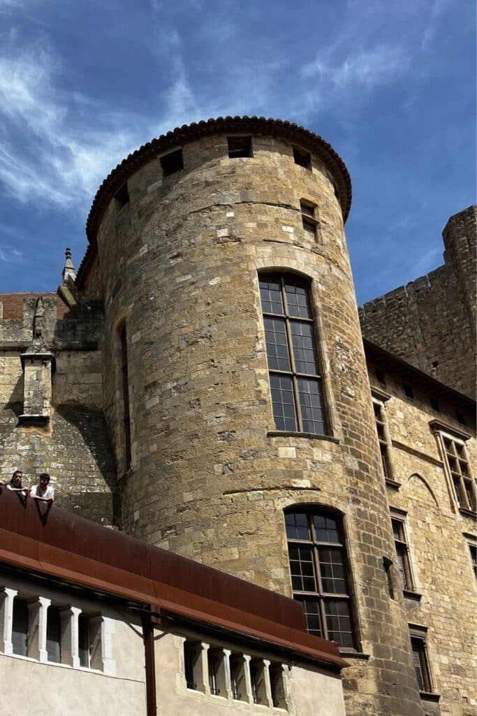 Close-up of a round stone tower at the Donjon Gilles Aycelin, with small windows and medieval architecture against a blue sky.