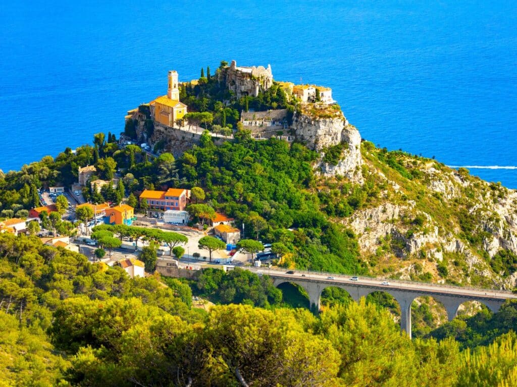 A picturesque hilltop village perched above the Mediterranean Sea, featuring ancient stone buildings and lush greenery—one of the hidden gems in the South of France.