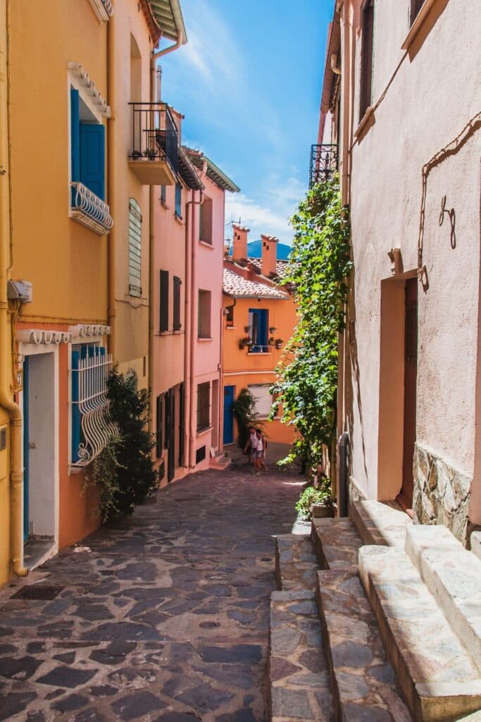 Vibrant orange and pink houses along a cobblestone street in Roussillon, framed by Mediterranean architecture and rich greenery, a hidden gem in the South of France.