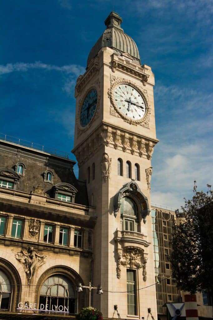 The iconic clock tower of the Gare de Lyon in Paris, standing tall against a clear blue sky. The building’s intricate architectural details showcase the elegance of this historic train station.
