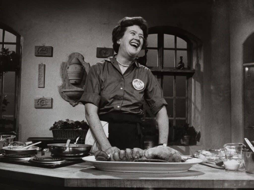A black and white picture of Julia Child, TV Chef and author in her studio kitchen smiling about to cook. Julia Child quotes were famous