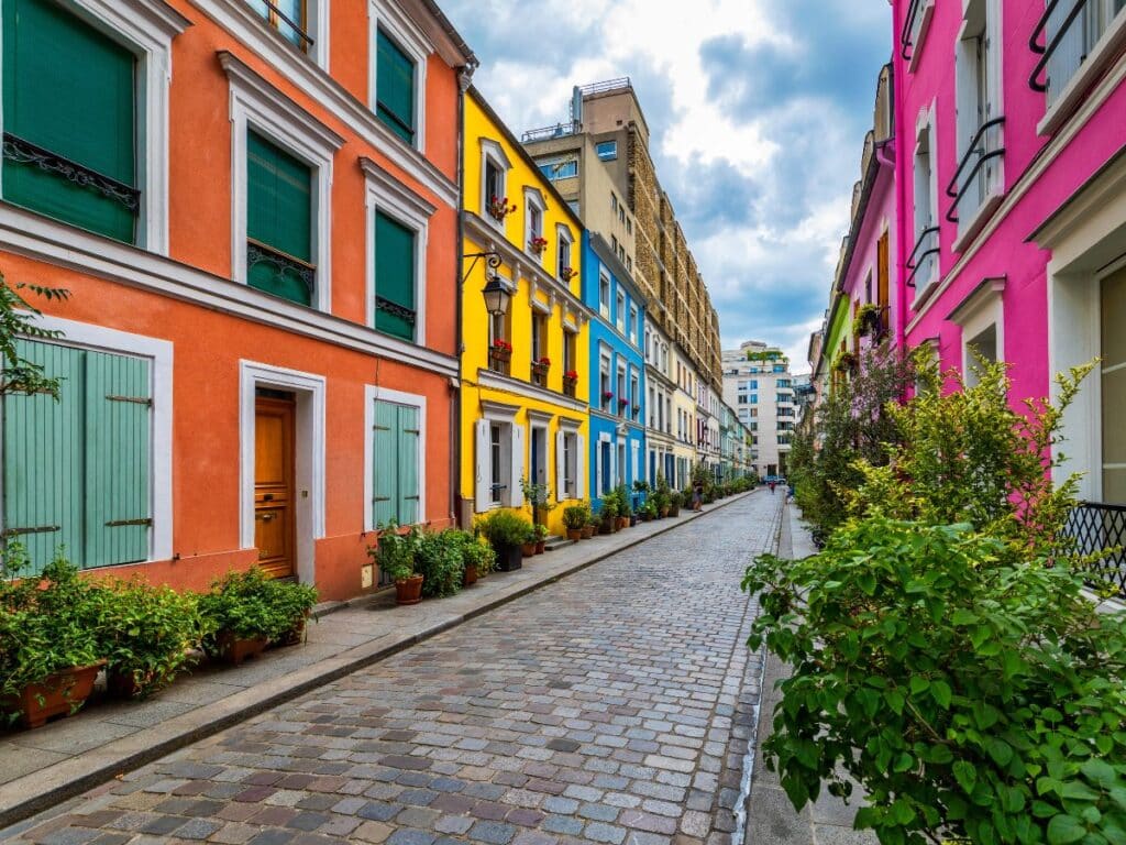 Another colorful view of Rue Crémieux, showcasing the street’s vibrant transformation. The houses are painted in striking hues like pink, blue, yellow, and orange, with lush greenery decorating the walkway.