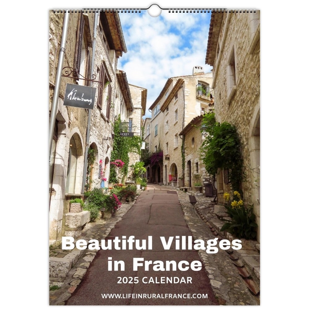 The cover of the "Beautiful Villages in France 2025 Calendar" showcases a picturesque stone-paved village street lined with rustic stone buildings adorned with vines and flowers, under a bright blue sky.