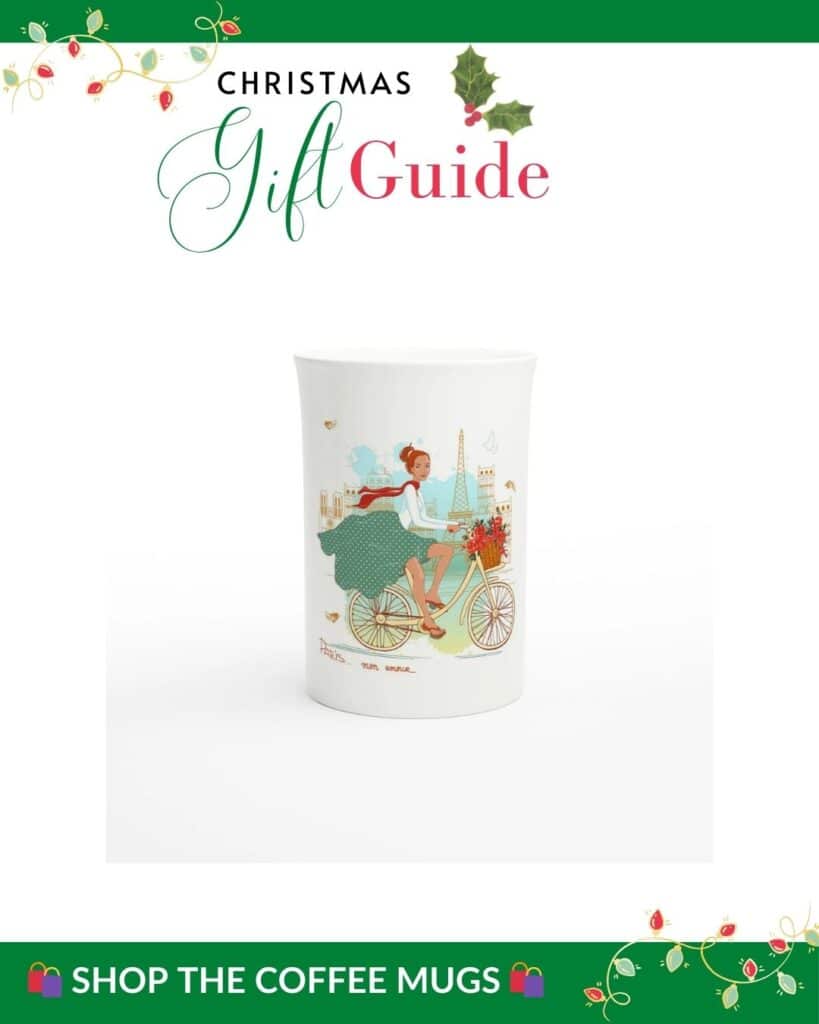 A holiday-themed graphic for a "Christmas Gift Guide" displays a white mug featuring an illustration of a woman in Paris riding a bicycle with a flower basket, with the Eiffel Tower and Parisian landmarks in the background. The text encourages shoppers to "Shop the Coffee Mugs."