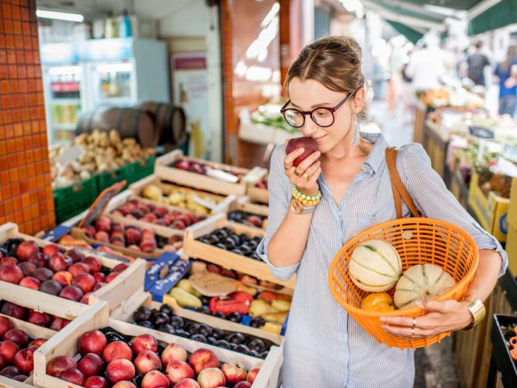 A woman at a French market compares fresh fruits, highlighting affordable local produce – a glimpse into the cost of living that appeals to Americans moving to France.