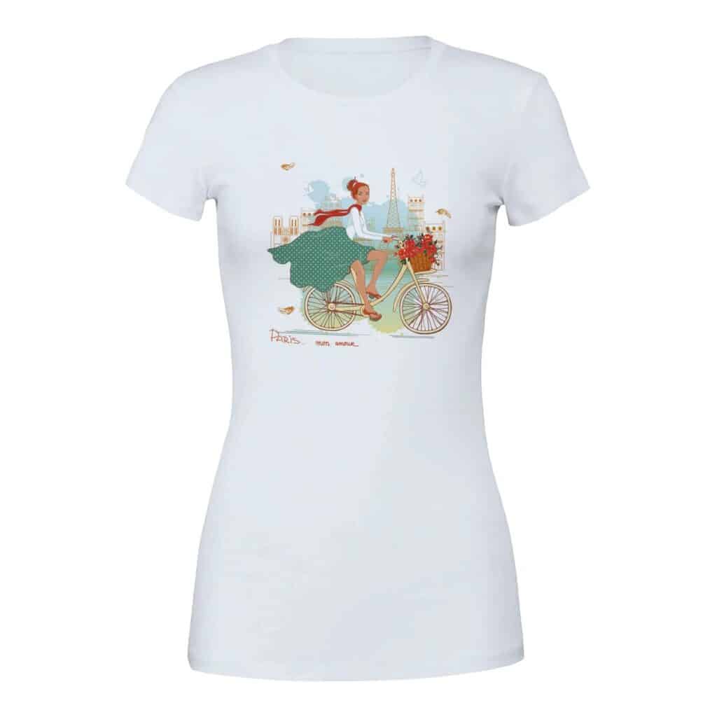 A white t-shirt featuring a charming illustration of a woman cycling in Paris, with landmarks like the Eiffel Tower in the background. The design includes a floral basket on the bike and the phrase "Paris mon amour," evoking a romantic, whimsical vibe.