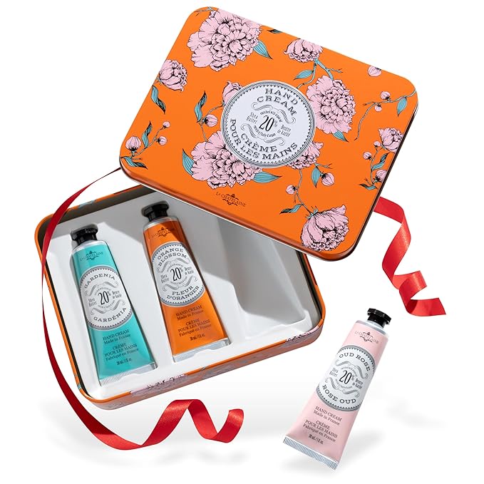 Another hand cream set displayed in an elegant orange tin with floral accents, featuring three rich creams in scents like Gardenia, Fleur d’Oranger, and Oud Rose. The packaging is festive with a red ribbon, making it a perfect gift option.