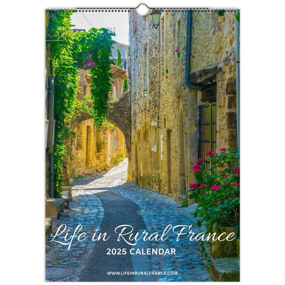 The "Life in Rural France 2025 Calendar" cover features a charming, sunlit French village alley, with cobblestone paths, lush green vines, and vibrant flowers climbing along rustic stone walls, capturing the serene beauty of rural France.