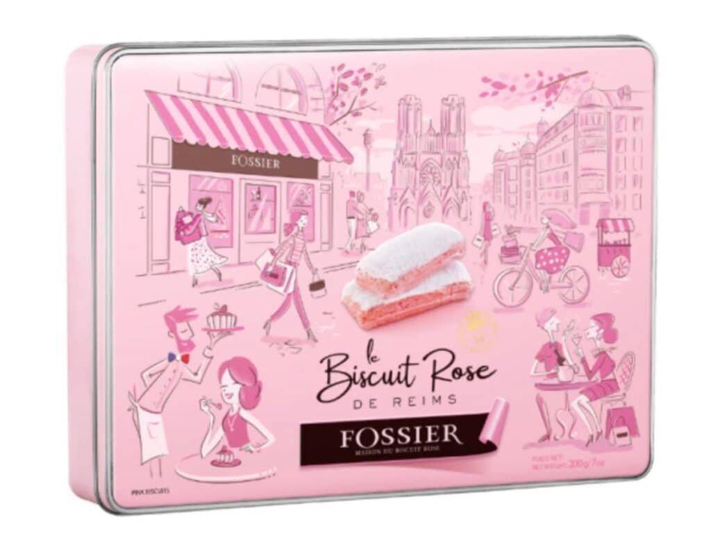 A pink metal tin decorated with Parisian-style illustrations, featuring two famous pink Reims biscuits on the lid, symbolizing a classic French treat.
