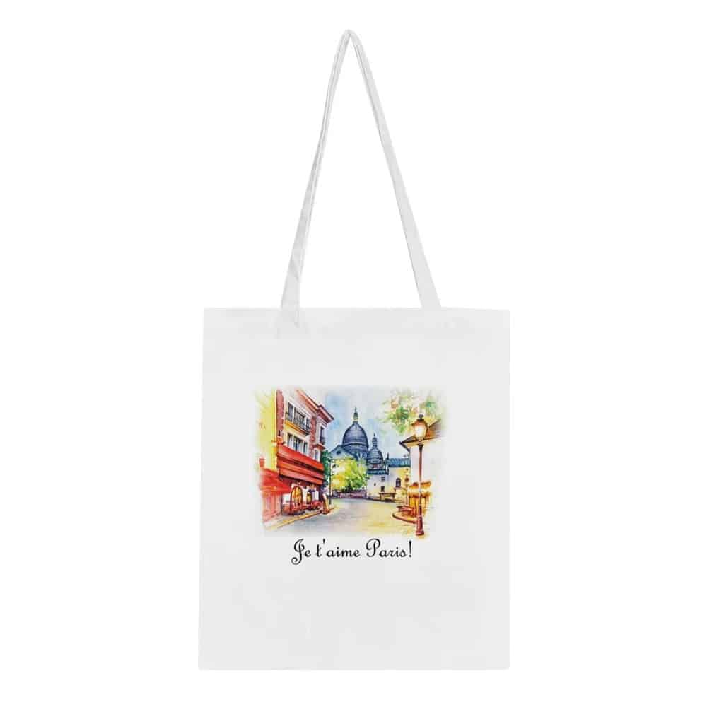 Another white tote bag displays a watercolor-style image of a picturesque Parisian street with a view of the Sacré-Cœur Basilica in the background, complemented by the phrase "Je t'aime Paris!" to celebrate a love for the city.
