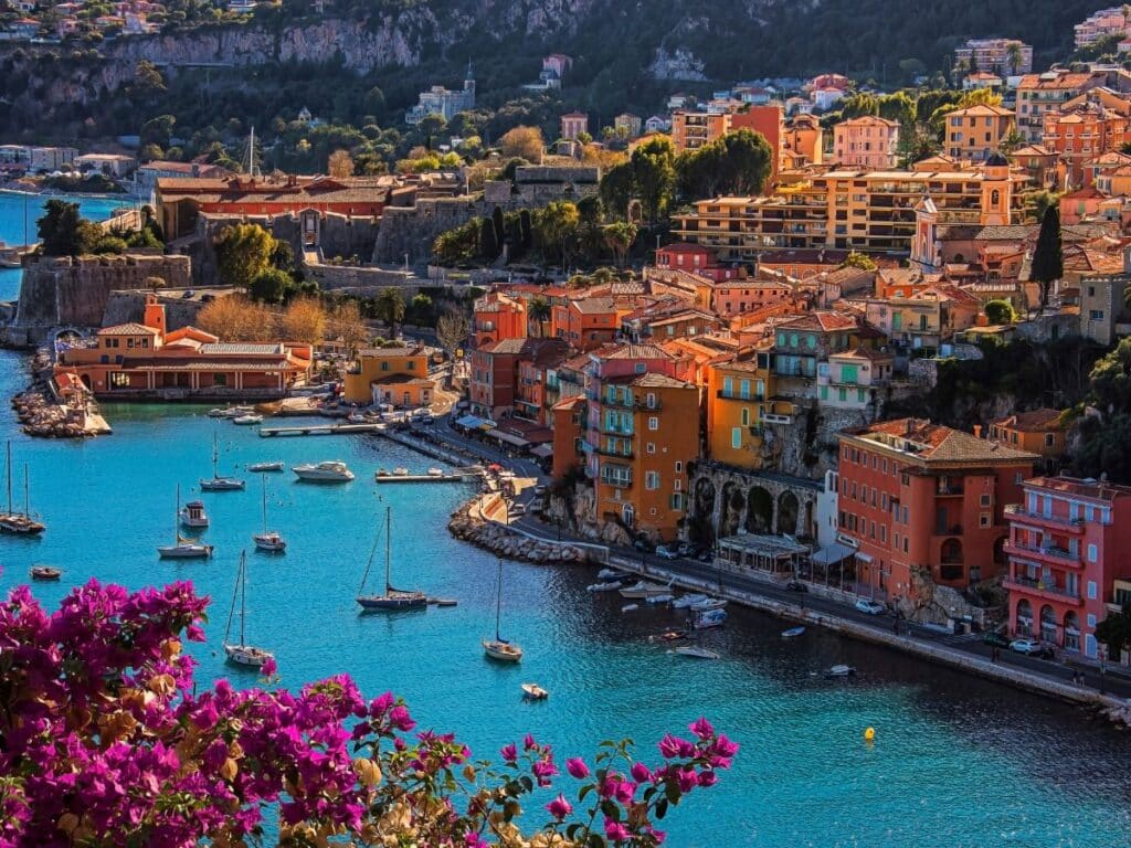 A stunning waterfront view of Villefranche-sur-Mer with colorful houses and anchored boats reflecting in the tranquil blue waters, perfect for Instagram.