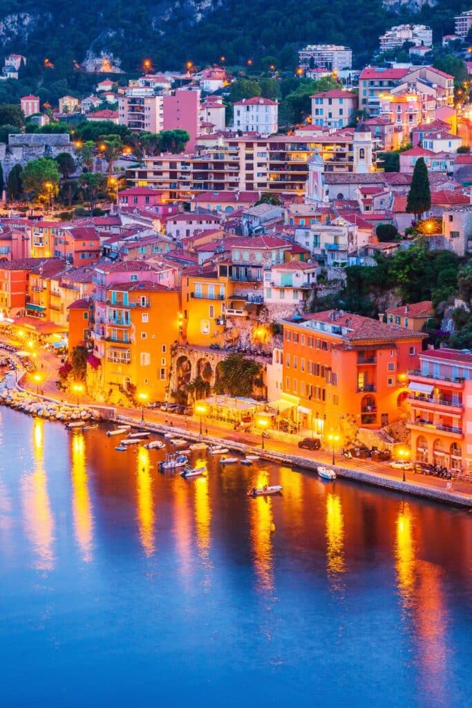 A panoramic view from La Terrasse du Soleil, capturing the serene bay and the colorful town of Villefranche-sur-Mer under a bright blue sky.