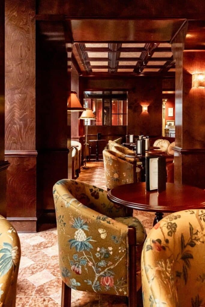 The cozy lounge at Le Procope, Paris's oldest café, featuring rich wood décor, floral-patterned chairs, and warm ambient lighting.
