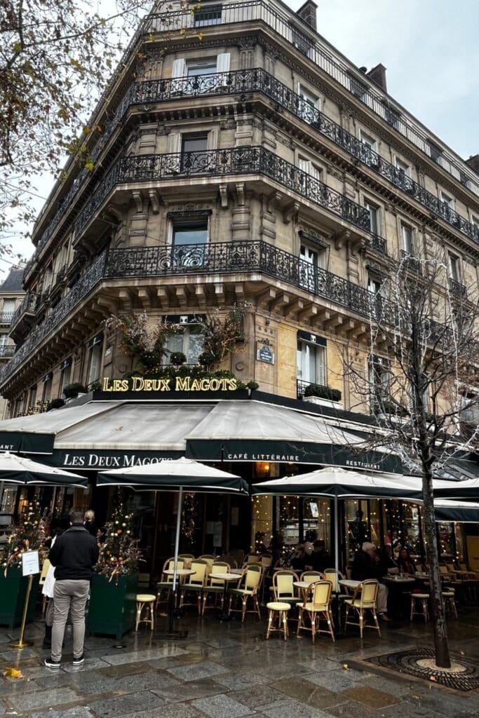The exterior of Les Deux Magots café, a historic Parisian landmark with green awnings, outdoor seating, and a classic façade.