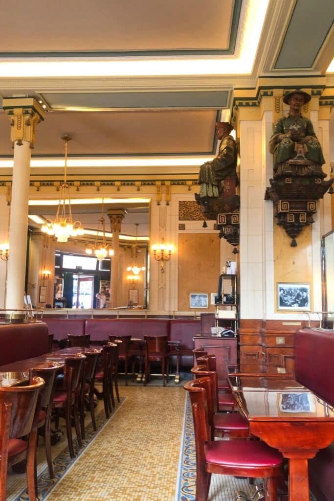 The ornate interior of Les Deux Magots café in Paris, featuring intricate columns, red leather seating, and historical décor.