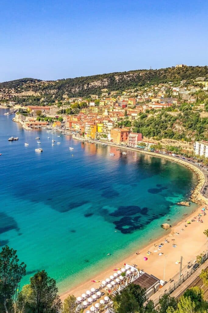 The sandy Plage des Marinieres beach in Villefranche-sur-Mer with turquoise waters and sun loungers, ideal for capturing tranquil seaside vibes.
