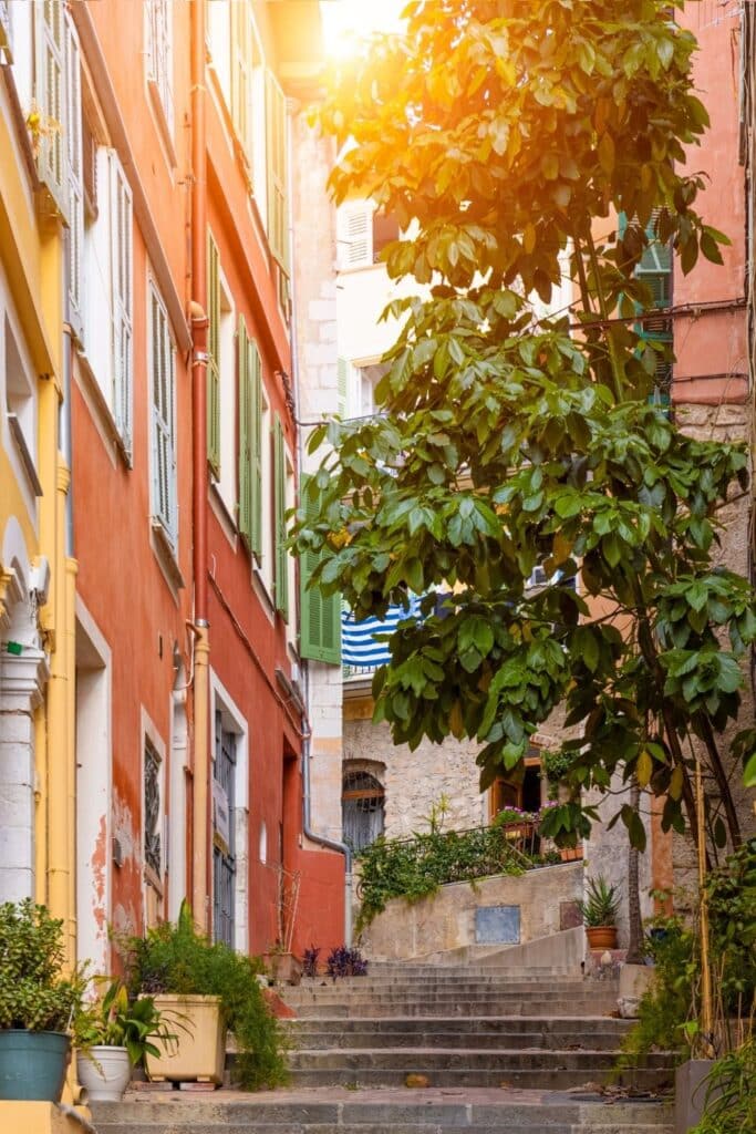 A charming staircase in Villefranche-sur-Mer’s old town, framed by vibrant houses with colorful shutters and lush greenery, offering a perfect setting for Instagram-worthy shots.