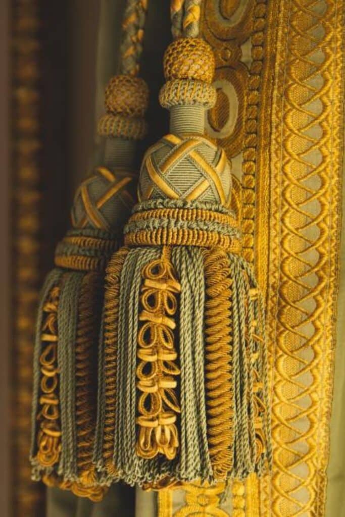 Detailed view of opulent curtain tassels with gold and green threads, intricate knots, and ornate braiding, emphasizing luxury craftsmanship.