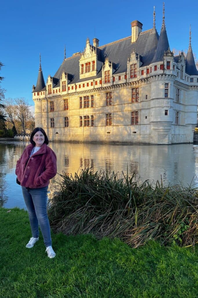 A photo of a visitor posing in front of the picturesque Chateau Azay le Rideau, with its sunlit facade and Renaissance-style architecture reflected in the moat.