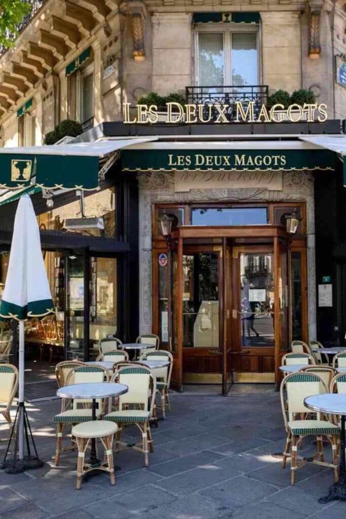 The historic Les Deux Magots café in Paris, featuring its elegant green awning, gold-lettered signage, and classic wicker chairs on the outdoor terrace, capturing the charm of Parisian café culture.