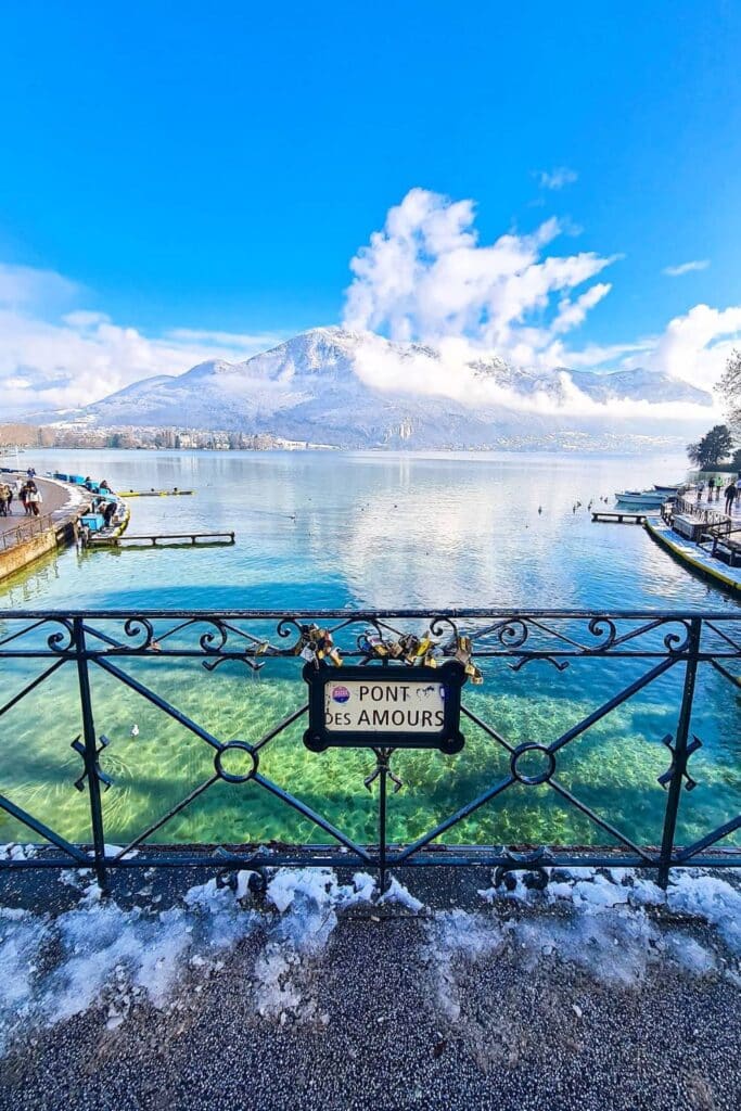 The Pont des Amours in Annecy with love locks on its railings, overlooking the pristine lake and snow-capped mountains.