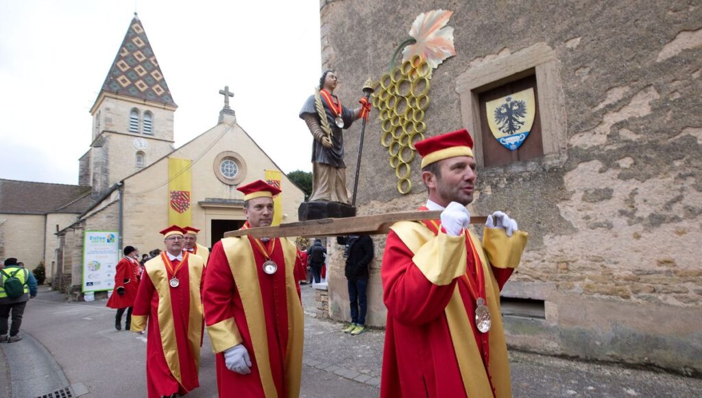 Participants dressed in vibrant red and gold robes carry a statue of Saint Vincent through a village during the Saint-Vincent Tournante, a traditional wine festival held every January in France to honor the patron saint of winemakers.