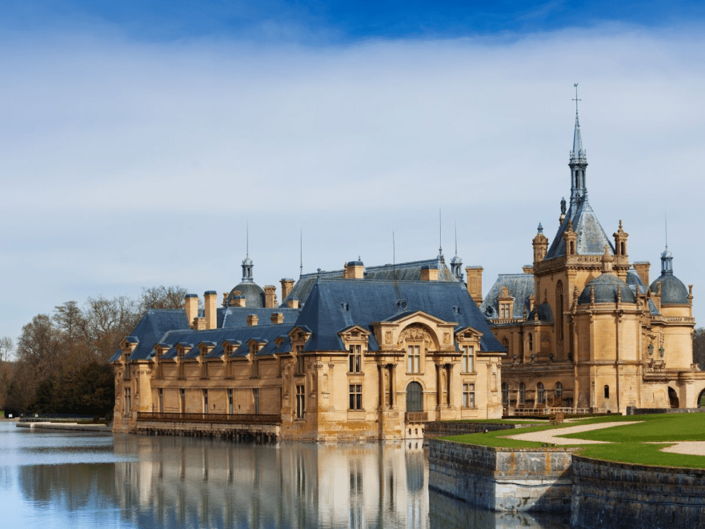 Château de Chantilly reflected in a moat under a blue sky, showcasing its detailed French Renaissance architecture. A top choice for day trips from Paris in 2025.
