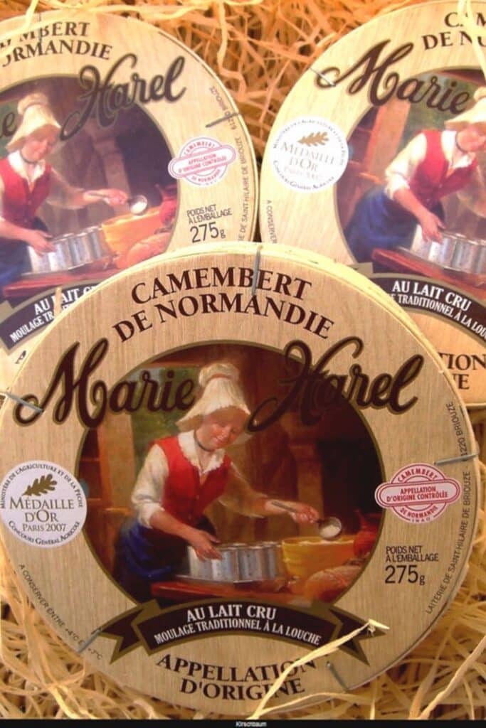 Traditional wooden boxes of Camembert de Normandie with vintage-style labels featuring a woman pouring milk, emphasizing the cheese’s artisanal heritage.
