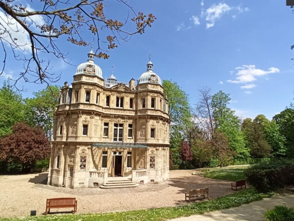 Majestic view of Château de Monte-Cristo with its ornate façade, domed towers, and detailed stone carvings, set against a clear blue sky and surrounded by verdant trees, showcasing its architectural splendor.