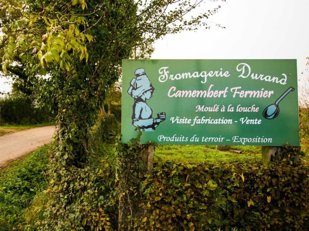 A countryside sign reading "Fromagerie Durand Camembert Fermier," marking a stop along the Normandy cheese route for camembert cheese enthusiasts.